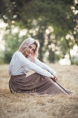 Wall Mural - young beautiful woman in a long dress on a background of dry grass sitting on glade in the forest, romantic girl relaxing alone in nature, natural female portrait