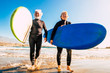 © Daniel - couple of seniors at the beach with black wetsuits holding a surftable ready to go surfing a the beach - active mature and retired people doing happy activity together in their vacations or freetime