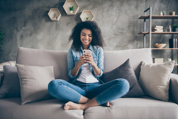 Poster - Photo of pretty dark skin curly lady homey domestic texting telephone with friends reading instagram comments sitting comfy couch casual denim outfit living room indoors