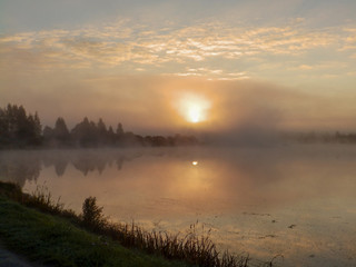 Wall Mural - Beautiful, colorful landscape of a foggy lake during sunrise. Misty dawn in the lake. Bright sun over lake.