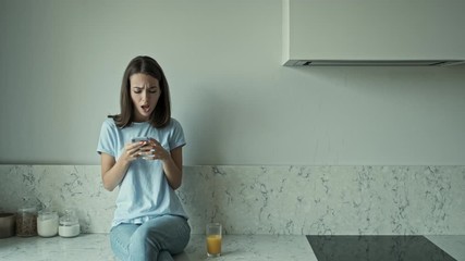 Wall Mural - Pleased pretty young brunette woman listening music with headphones on smartphone and singing while sitting at the kitchen at home