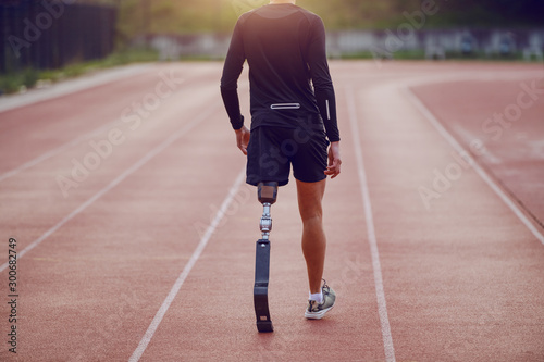 Cuadros en Lienzo Rear view of handsome caucasian handicapped young man with artificial leg and dressed in shorts and sweatshirt walking on racetrack