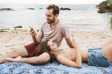 Wall Mural - photo of cheerful young couple using cellphones and smiling