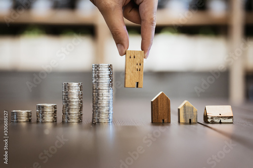 Hand choosing mini wood house and row of coin money on wood table and , selective focus, Planning to buy property. Choose what\'s the best. A symbol for construction ,ecology, loan concepts