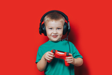 Wall Mural - little boy in headphonesplaying computer game with gamedas in hands on red background.