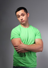 Thinking casual doubt young man with folded arms in green shirt on grey backgrond.