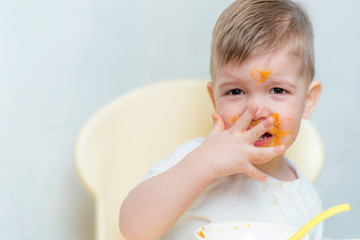 cute baby boy while eating smeared his face with a pumpkin