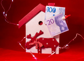 Swedish banknotes as part of Christmas decoration with Christmas tree and moose in front of red background