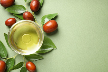 Glass bowl with jojoba oil and seeds on green background, flat lay. Space for text