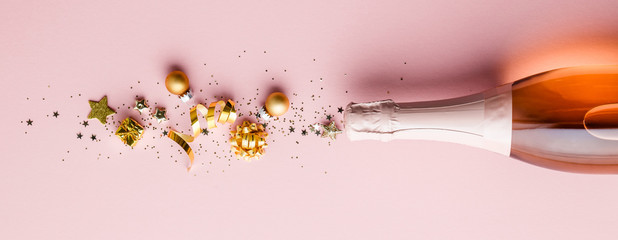 Flat lay of Celebration. Champagne bottle and golden decoration on pink background