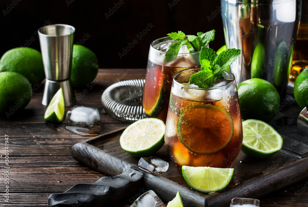 Cuba libre alcohol cocktail with golden rum, lemon juice, cola, lime and ice, dark bar counter background, bar tools, place for text - obrazy, fototapety, plakaty 