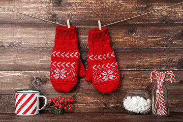 Wall Mural - Knitted mittens with candies, marshmallow and striped mug on brown wooden background