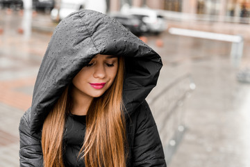 beautiful girl with makeup in a black jacket in a hood under the rain