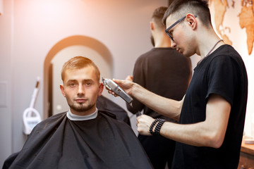 Uzbek hairdresser cuts a young handsome guy in a barbershop, a male client sits in a beauty salon and makes a short haircut