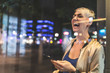 © WILLIAM PERUGINI/Westend61 - Portrait of laughing blond woman using mobile phone at night, Berlin, Germany