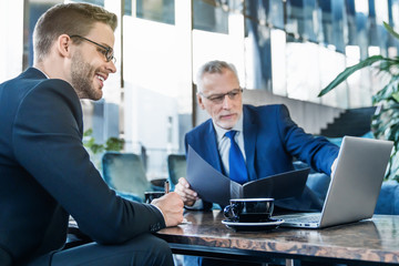 Two businessmen using laptop in lobby of modern office