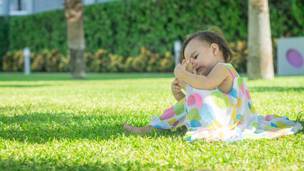 Little girl in colorful dress sitting on the grass