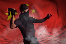 A Man In Black Throws A Burning Bottle On The Background Of The Flag Of China. Studio Photography. Theme Of Street Protests