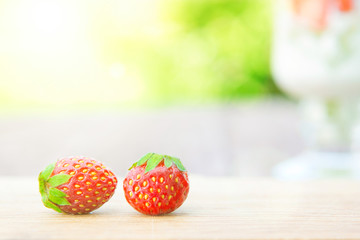 Two strawberryes on cutting board on wooden table over green sunny garden