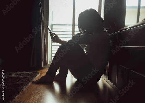 Cuadros en Lienzo Asian woman sitting on wood floor beside window light in a dark room