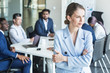 © xartproduction - Business woman stands on the background of partners. A team of young businessmen working and communicating together in an office. Corporate businessteam and manager in a meeting