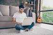 © deagreez - Photo of mixed race arabian guy sitting cozy floor carpet near sofa holding notebook speaking skype with relatives wear casual outfit flat loft living room indoors