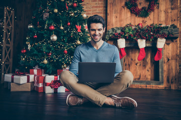 Full length body size photo of cheerful positive toothy beaming sitting on floor with legs crossed browsing through laptop in beige pants trousers footwear beige