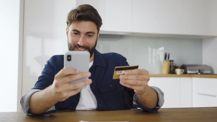 Wall Mural - Young man paying with phone and credit card for online shopping at home