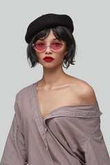 Wall Mural - Medium shot of a brunette girl in a striped shirt, black beret and cat eyes retro sunglasses with a transparent half-frame and reddish lens. The photo is made on the gray background.