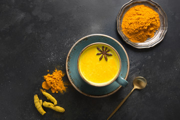 Wall Mural - Cup of ayurvedic golden turmeric milk with curcuma powder and anise star on black. View from above.