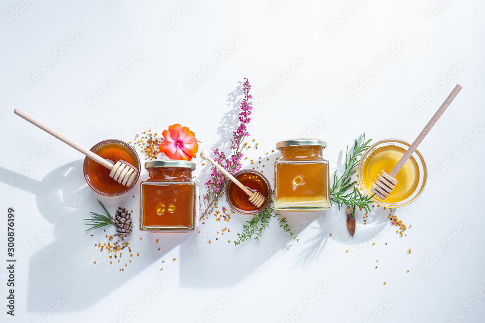 Composition of honey  jars with honey sticks ,flowers and bee pollen on white background - obrazy, fototapety, plakaty 