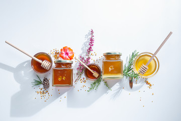 composition of honey jars with honey sticks ,flowers and bee pollen on white background