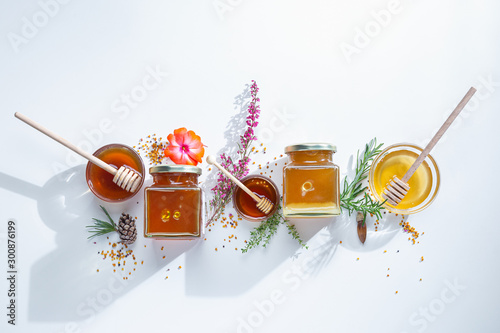 Fotografía Composition of honey jars with honey sticks ,flowers and bee pollen on white ba