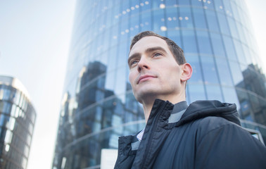 Portrait of a proud successful self-confident guy, young businessman outdoors in background of modern office business centre. Thinking, dreaming about future good career. Purposeful satisfied employee