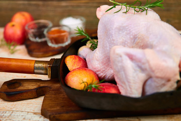 Wall Mural - Whole raw chicken in skillet  or iron pan with rosemary leaf, thyme, lemon, red apples . Ready to cook. Cooking background. Copy space