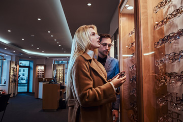 Wall Mural - Shop assistant with woman client choosing eyeglasses at glasses store.