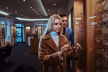 Poster - Shop assistant with woman client choosing eyeglasses at glasses store.