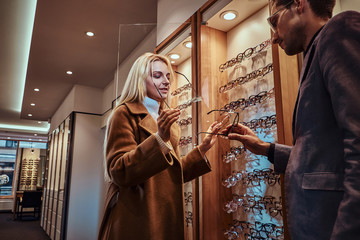 Sticker - Professional male consultant is helping to choose new glasses to female customer at optic shop.