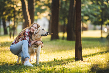 full length view of beautiful young girl in casual clothes hugging golden retriever while sitting on