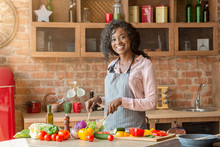 Joyful African Lady Mixing Veggies In Bowl In Kitchen