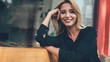 Close up portrait of pretty Caucasian woman with blonde hair taking rest on city bench and looking at camera with cute sincerely smile on face, positive hipster girl feeling good during free day