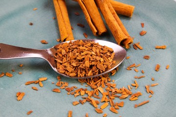 Close up of isolated spoon with crushed cinnamon and sticks on blue scratched china plate