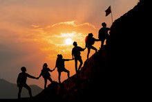 Silhouette Of People Helping Each Other Hike Up A Mountain At Sunset Background. Hiking, Business, Teamwork, Success, Help And Goal Concept.