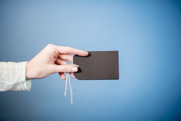 Canvas Print - Closeup shot of a female holding a blank black tag with a blue background - great for witting text