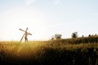 Beautiful shot of a male carrying a wooden cross in a grassy field with sun shining in background