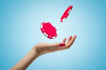 Poster - female hand throwing two red casino tokens up in the air on blue background