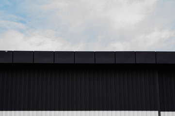 Black and white Corrugated metal sheet texture surface on a building wall with a cloudy sky. Galvanize steel background.