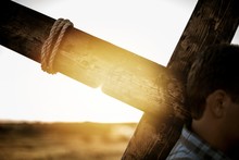 Closeup Shot Of A Male Carrying A Wooden Cross With The Sun Shining In The Background
