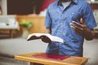 Closeup shot of a male reading the bible near a wooden stand with a blurred background