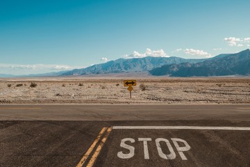 Wall Mural - road in the middle of the desert with a mountain range in the background under the blue sky